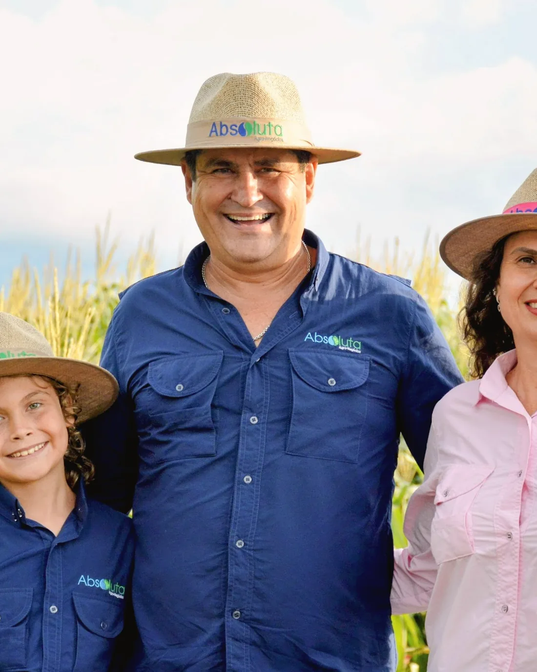 Casal e filha, de camisa da revenda, em pé num milharal